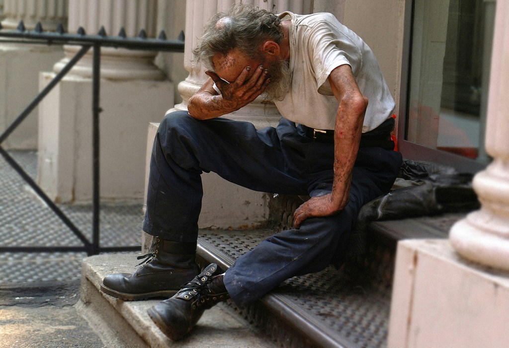 A homeless man sitting in short sleeves with his head in his hand